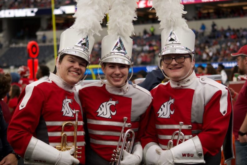 Three Cougar Marching Band members smile for a photo during a performance.