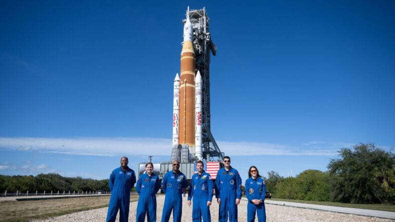 Astronauts pose in the foreground as the SLS rocket sits on its launch pad at Kennedy Space Center.