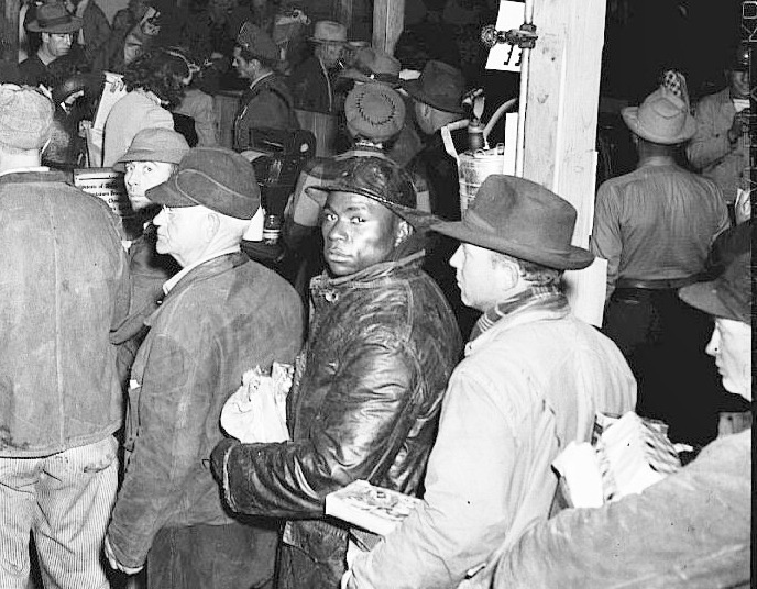 Crowd of white people and one black person looking at camera in line at grocery store in Hanford, 1944