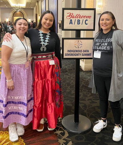 Cheryl Ellenwood and two WSU students standing next to a sign at the Indigenous Data Sovereignty Summit.