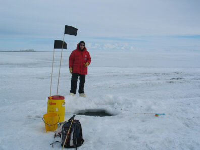 Wes Dowd stands on the Antarctic tundra near a hole broken in the ice among various gear.
