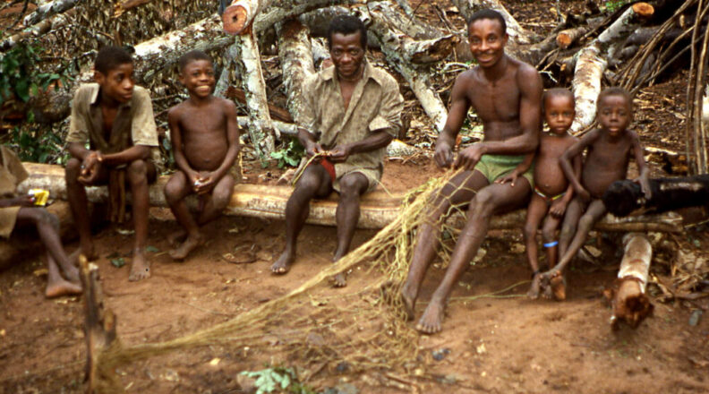 A man shows a group of children how to weave a hunting net.