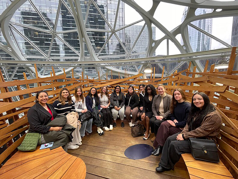 A group of students sit at a round bench inside the Amazon Spheres building in Seattle.