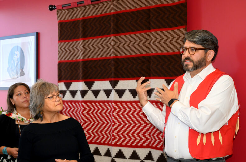 three people stand in front of a colorful blanket hanging on a wall