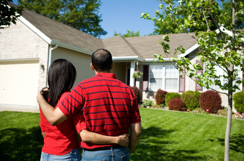 A couple standing with their arms around one another looking at a home.