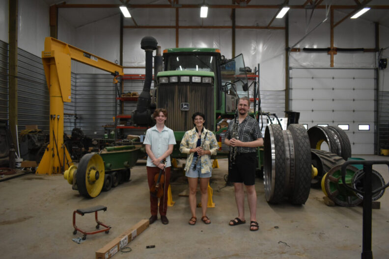 Alex Crisp, Calby Van Hollebeke, and Kamil Tarnawczyk pose in front of a tractor.