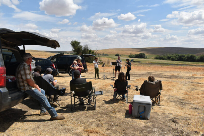 Members of the Miller family farm crew watch a performance of “Harvest Interludes” outside of LaCrosse, WA.
