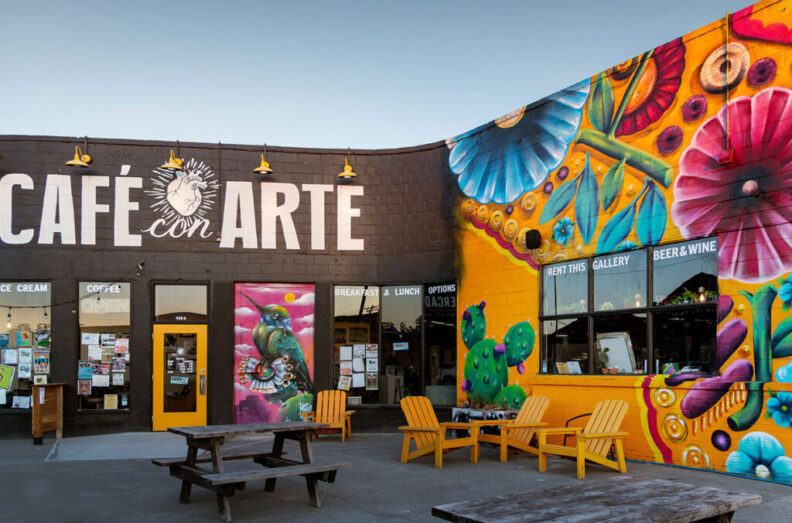 Adirondack chairs and picnic tables sit underneath a mural painted outside Café con Arte.