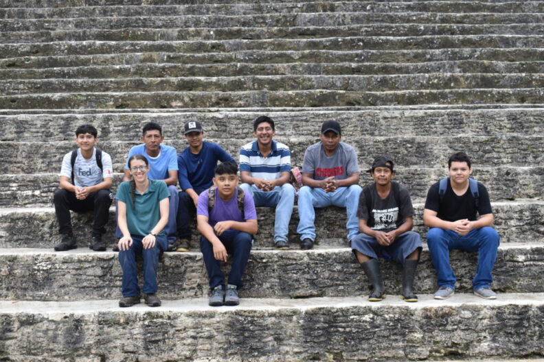 Nine members of an excavation team posing for a photo on the steps of a Maya pyramid.
