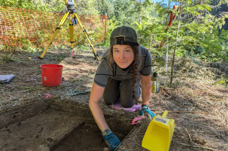 Jordan J. Thompson looking up while leaning over an excavation plot in the Bitterroot Mountains.