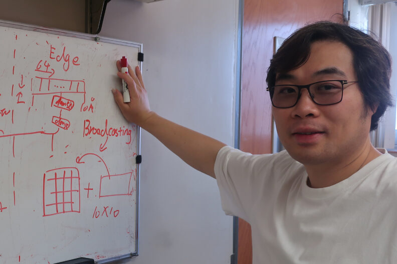 Juejing Liu, a postdoctoral researcher in chemistry, stands in front of a white board with red writing.