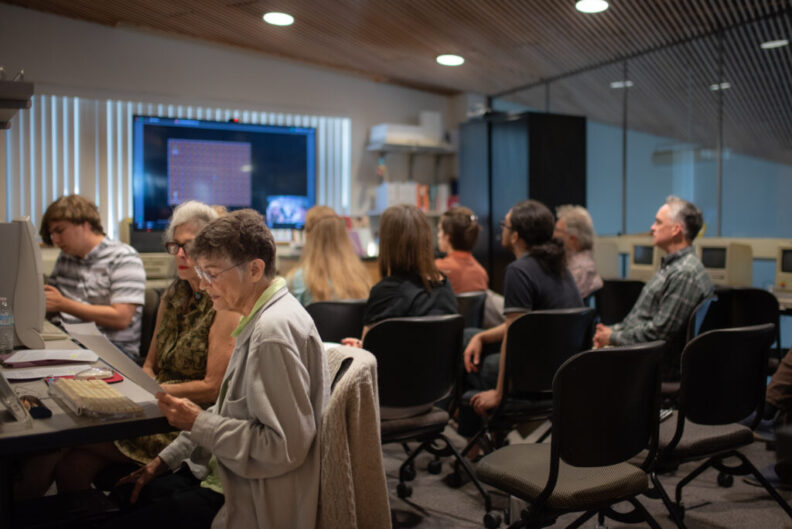 Several audience members are seated in a meeting space looking at a screen.