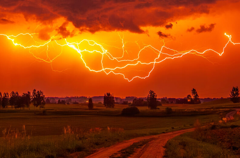 A lightning storm taking place against a dark red sky in the countryside.