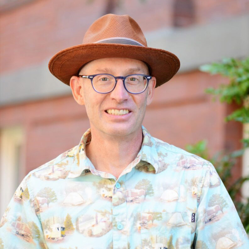 Kirk McAuley in a light-colored patterned shirt, wearing glasses and a hat.