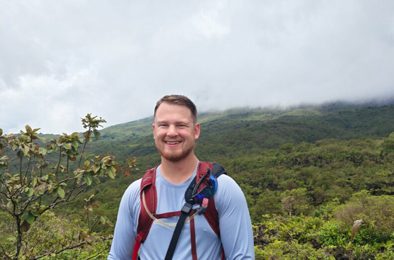 Closeup of John Balke standing in front of a forest covered mountain in Costa Rica.