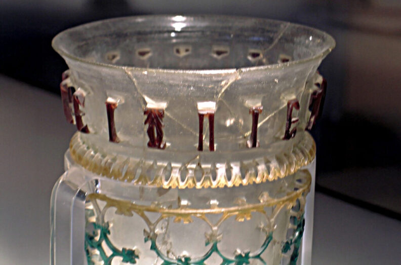 Closeup of a glass vessel from ancient Rome with an inscription engraved on it.