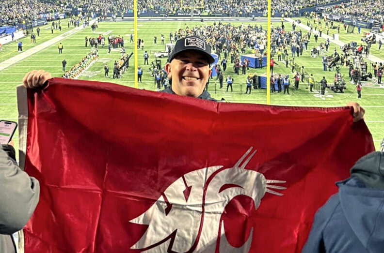 WSU alumnus Jason Fox holding a Cougar flag at a Seattle Seahawks football game.