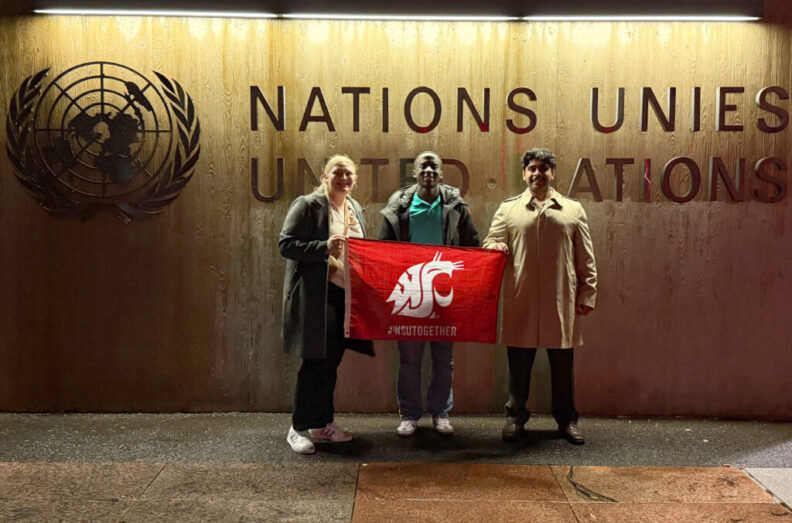 Three WSU students pose for a photo in front of a United Nations sign in Geneva holding a WSU flag.