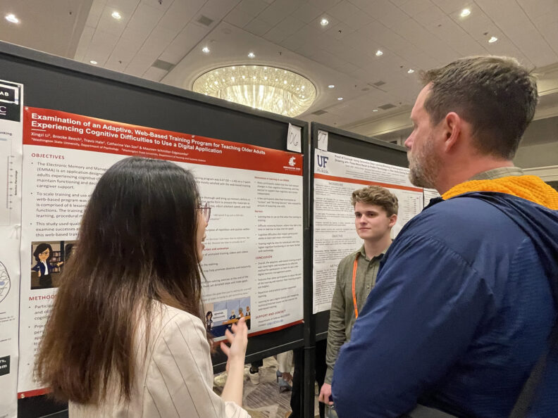 Two students at conference discussing poster presentation with a spectator.