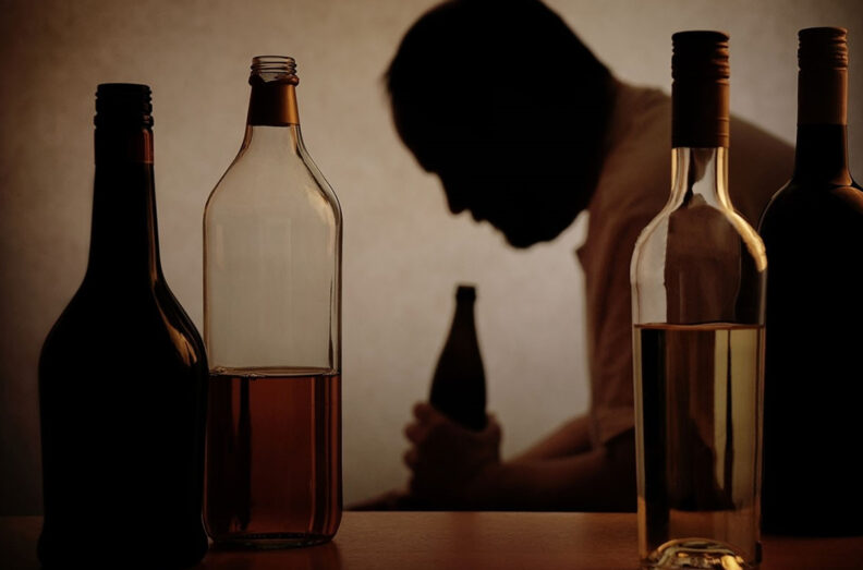 The silhouette of a man is seen behind an array of alcohol bottles.
