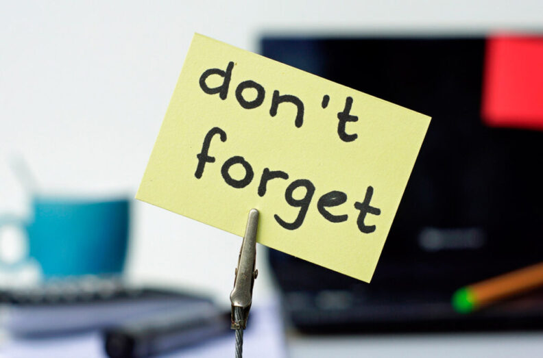 A sticky note that reads "don't forget" is held by an alligator clip in front of an office background.
