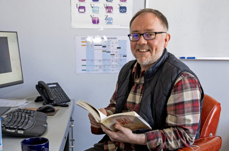 WSU professor Justin Denney sitting at a desk with an open book.
