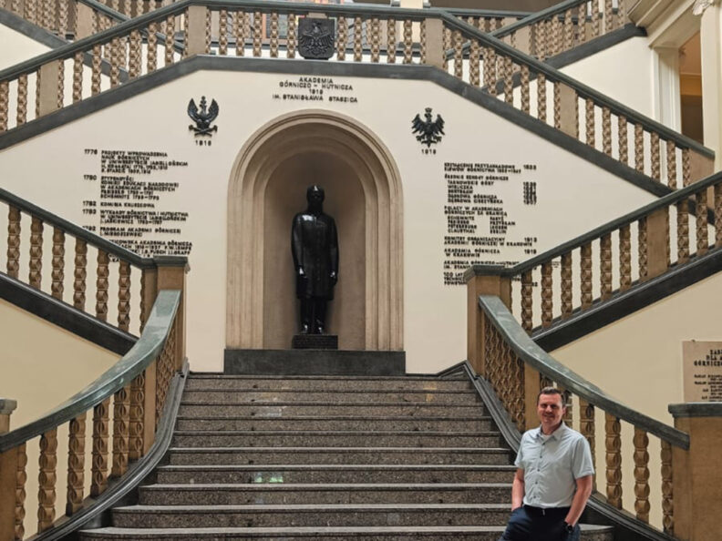 Sergey Lapin stands in the historical entrance of the AGH University of Kraków's Main Building.