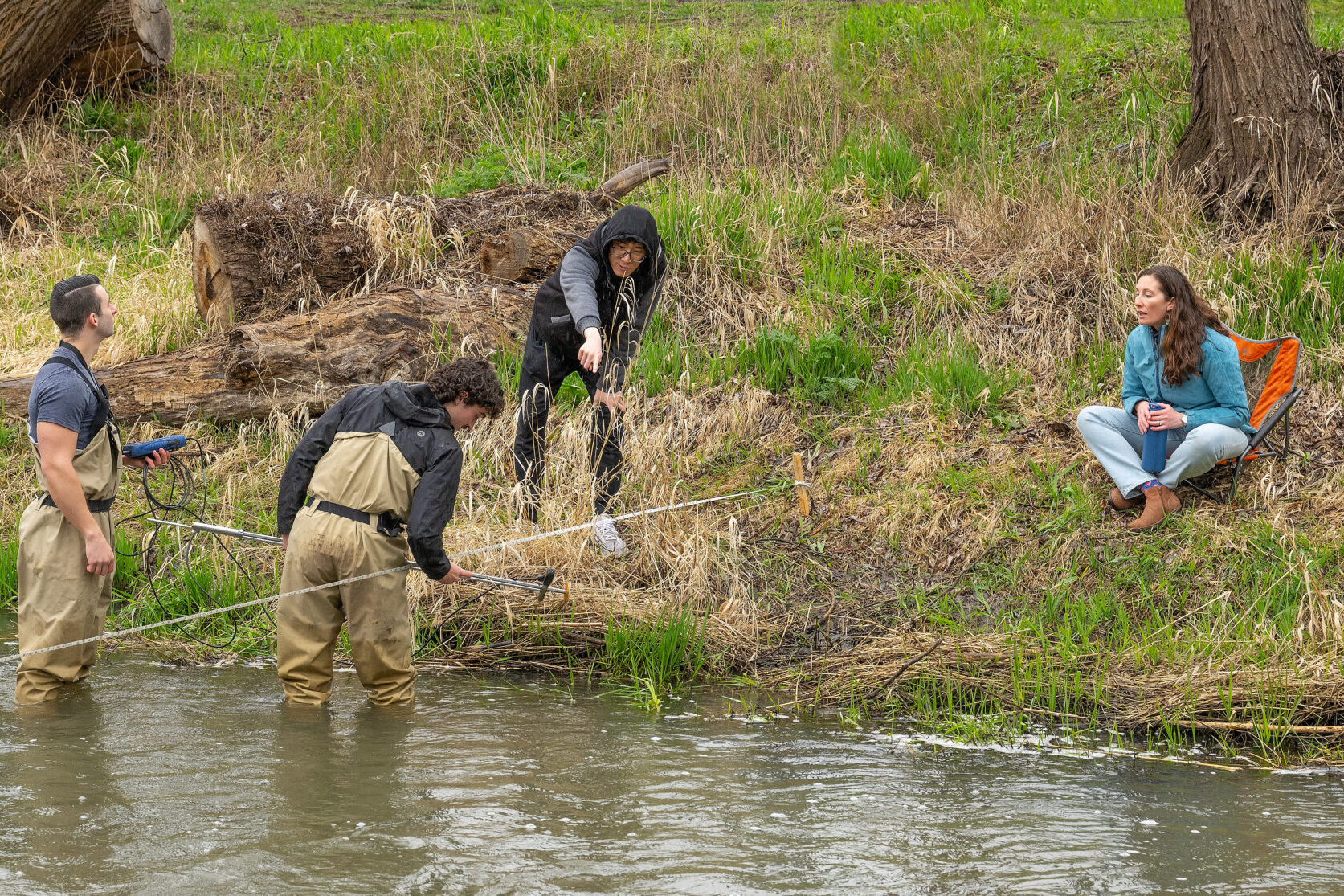 Students in protective clothing take water readings at the banks of a stream.