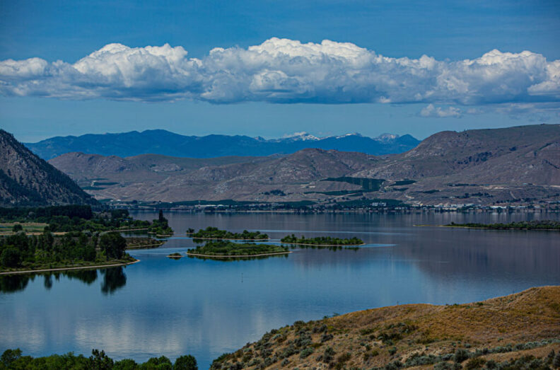 Image of serene lake with orchards and mountains in the background.
