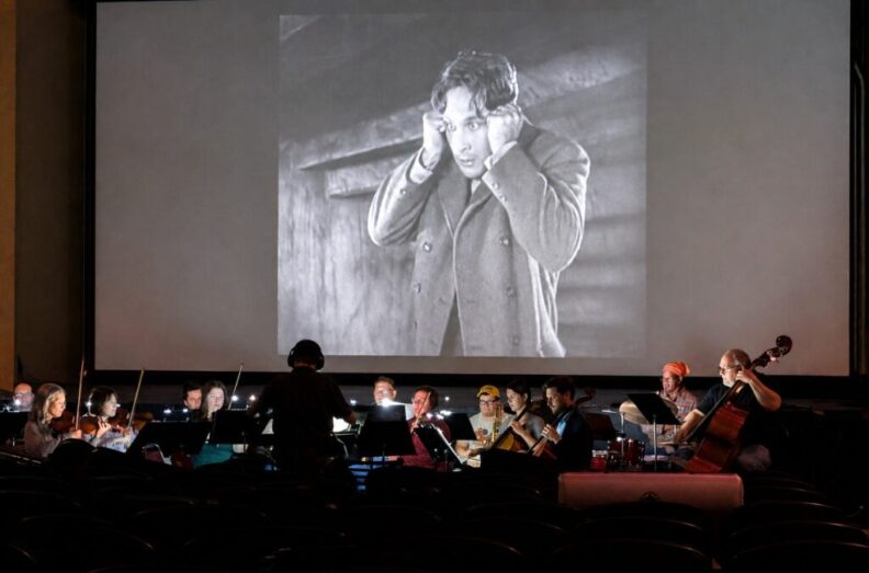 Musicians perform in a small pit in front of a silent movie.