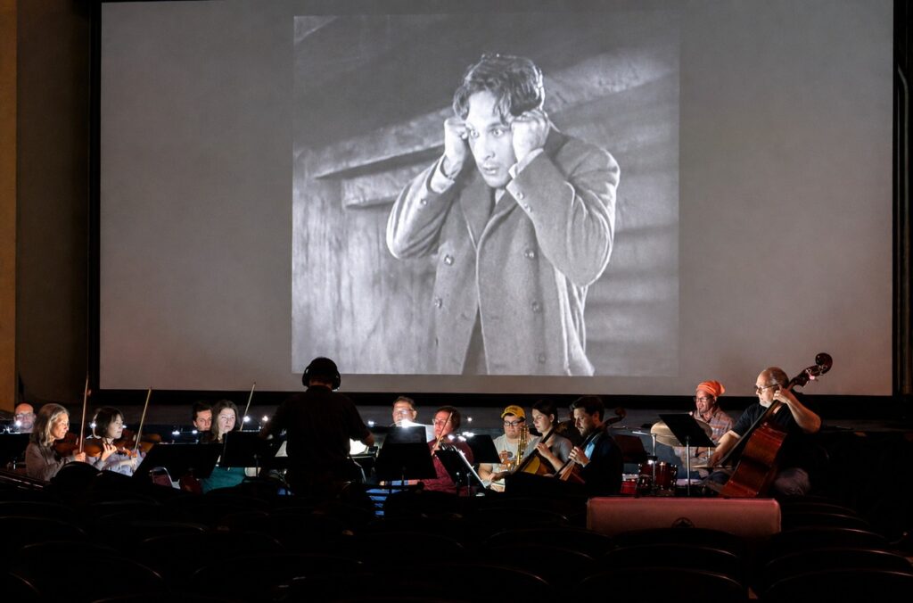 Musicians perform in a small pit in front of a silent movie.