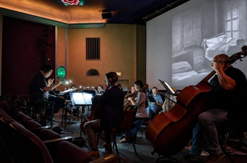 Musicians perform in front of a silent film. 