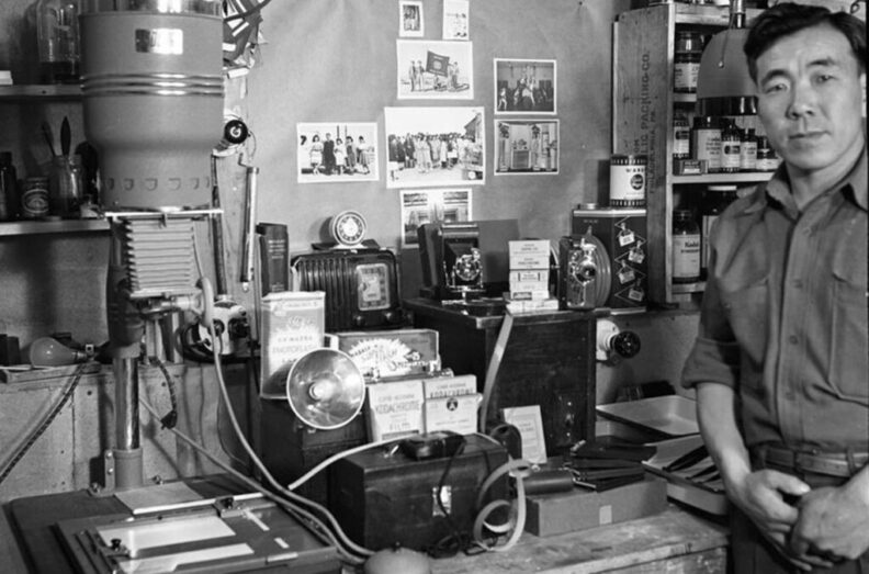 A man stands next to photography equipment in a historical photograph.