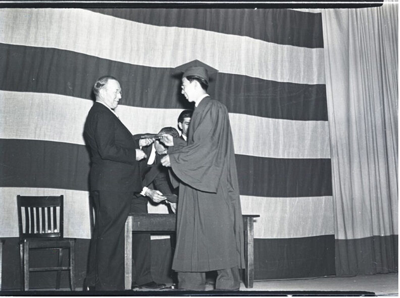 A man hands a younger man a diploma in a historic photo.