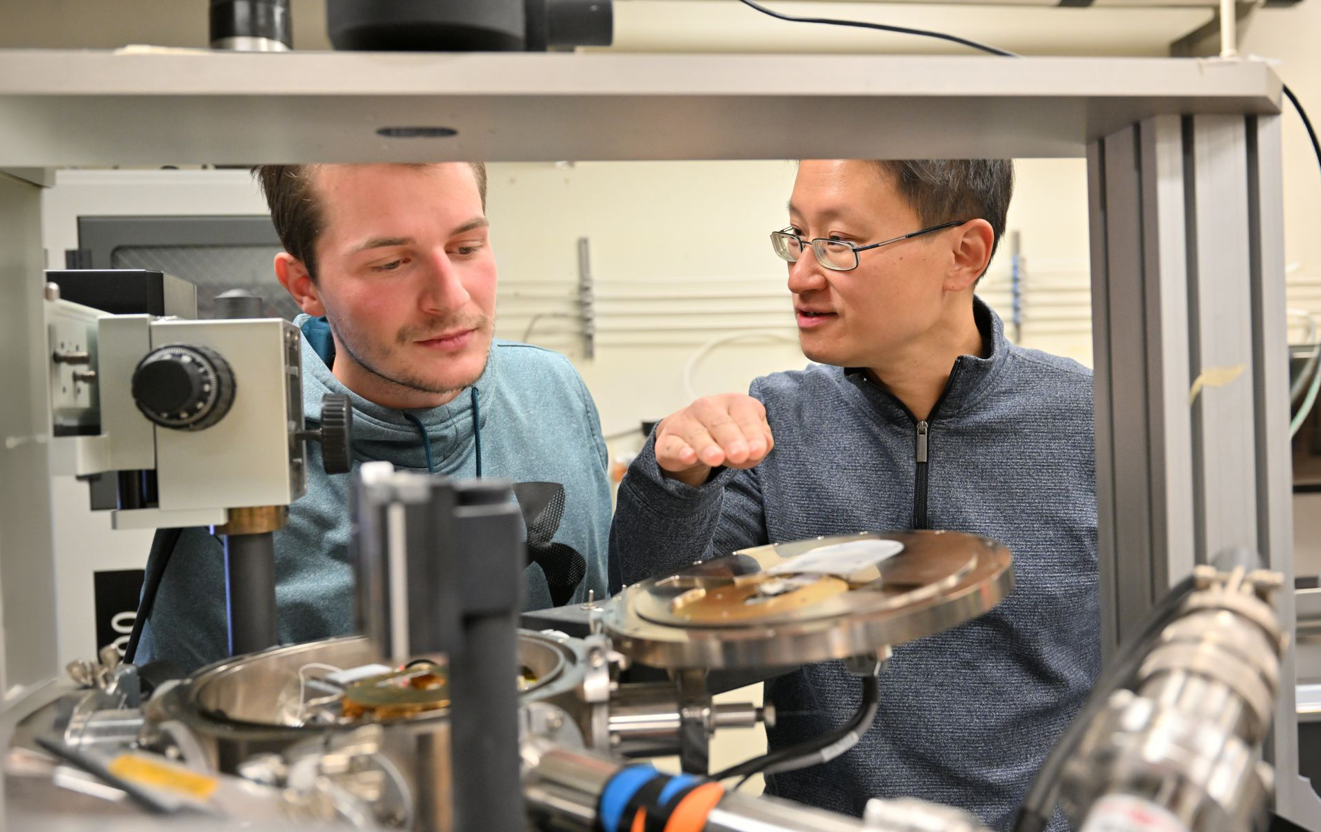 Professor Yi Gu with a graduate student having a discussion in the lab near equipment.