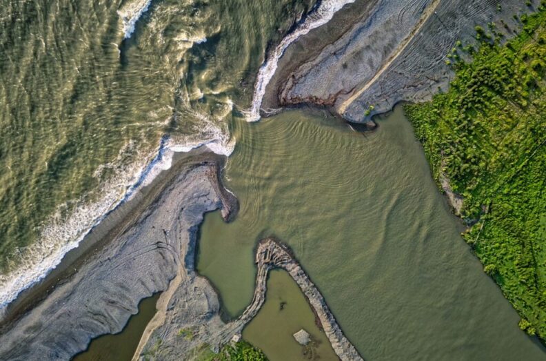 An aerial image shows river water flowing into the ocean.