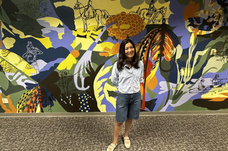 WSU Department of Art assistant professor Jiemei Lin stands in front of the mural she painted this past summer.