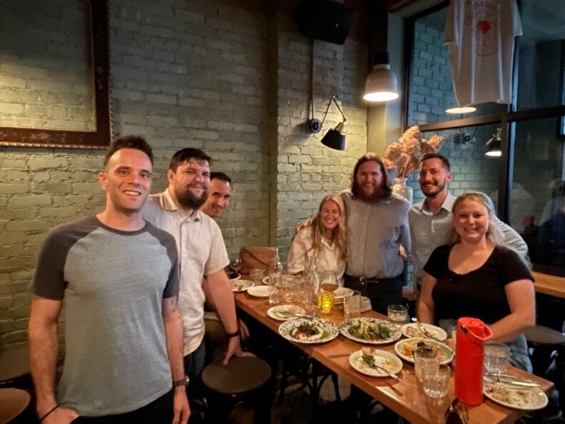 A group of people stand around a table with plates of food.