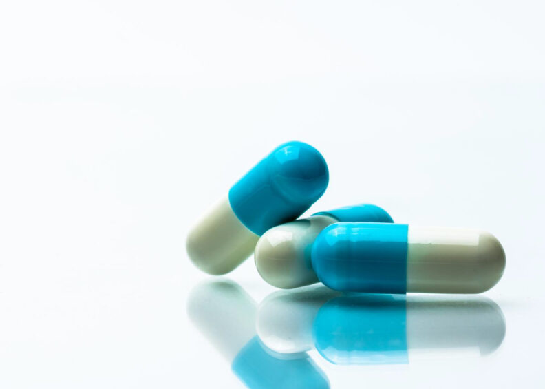 Blue and white pills on a reflective surface.
