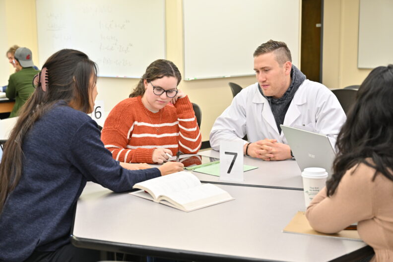 Students in the Math Learning Center meet with a lab instructor wearing a white lab coat.