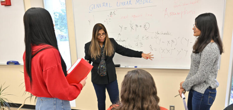 Jan Dasgupta working with students at a white board with mathematic equations. 