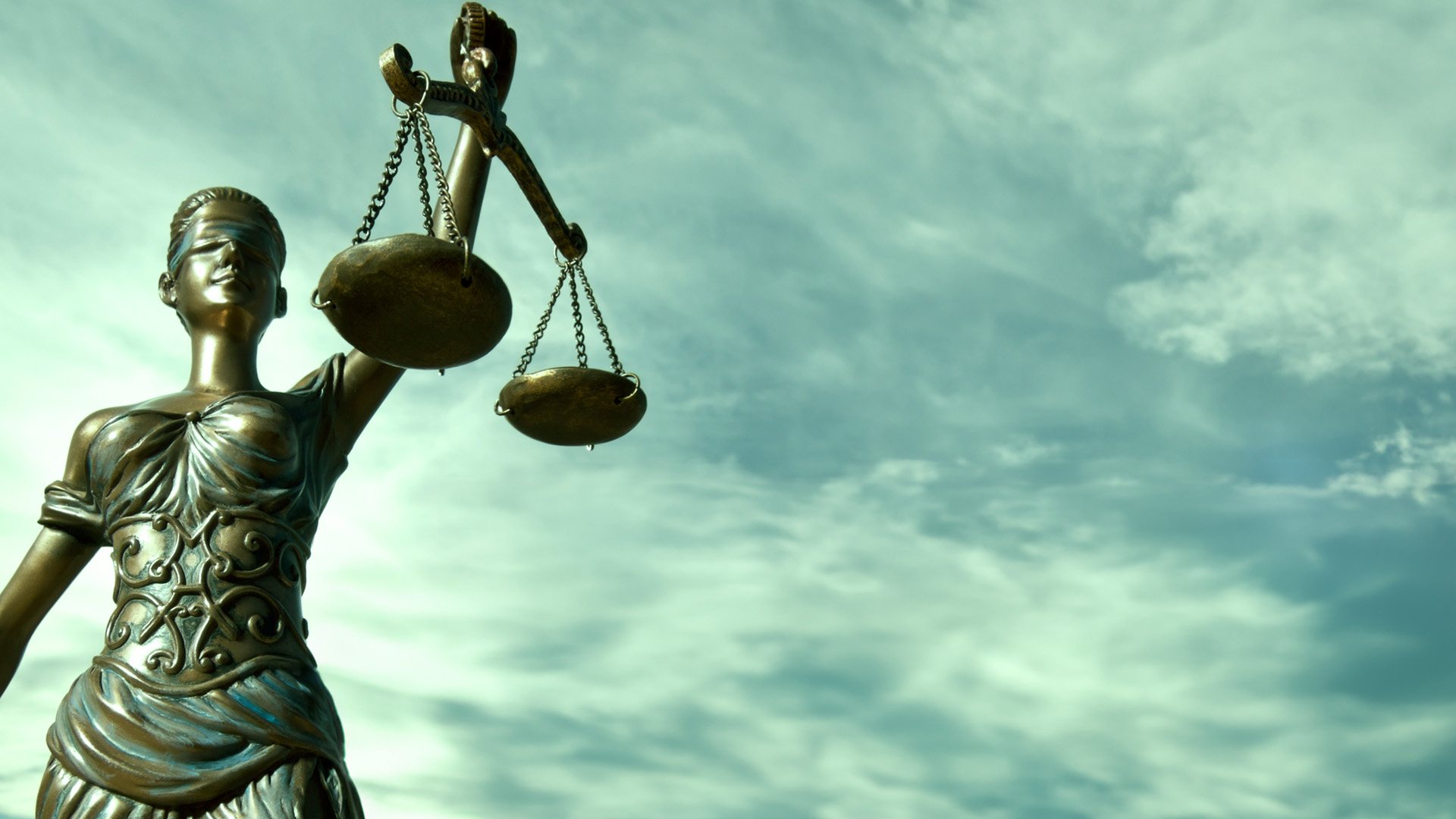 Sculpture of Justitia against a blue cloudy sky.
