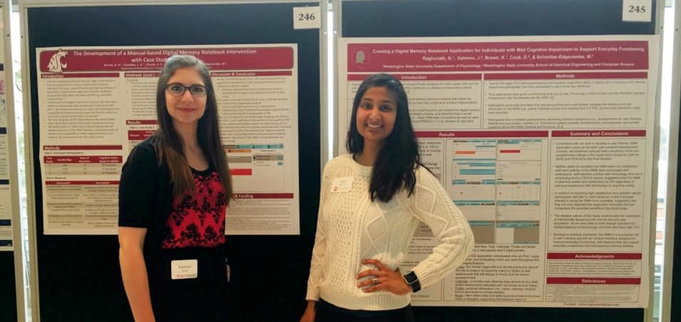Two women stand by academic posters, smiling