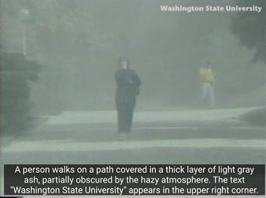 Video still showing a person walking on a pedestrian pathway covered in ash. "Washington State University" is printed in the top right, and a caption below reads, "A person walks on a path covered in a thick layer of light gray ash, partially obscured by the hazy atmosphere. The text Washington State University' appears in the upper right corner."
