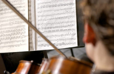 Person practicing violin with sheet music in background.