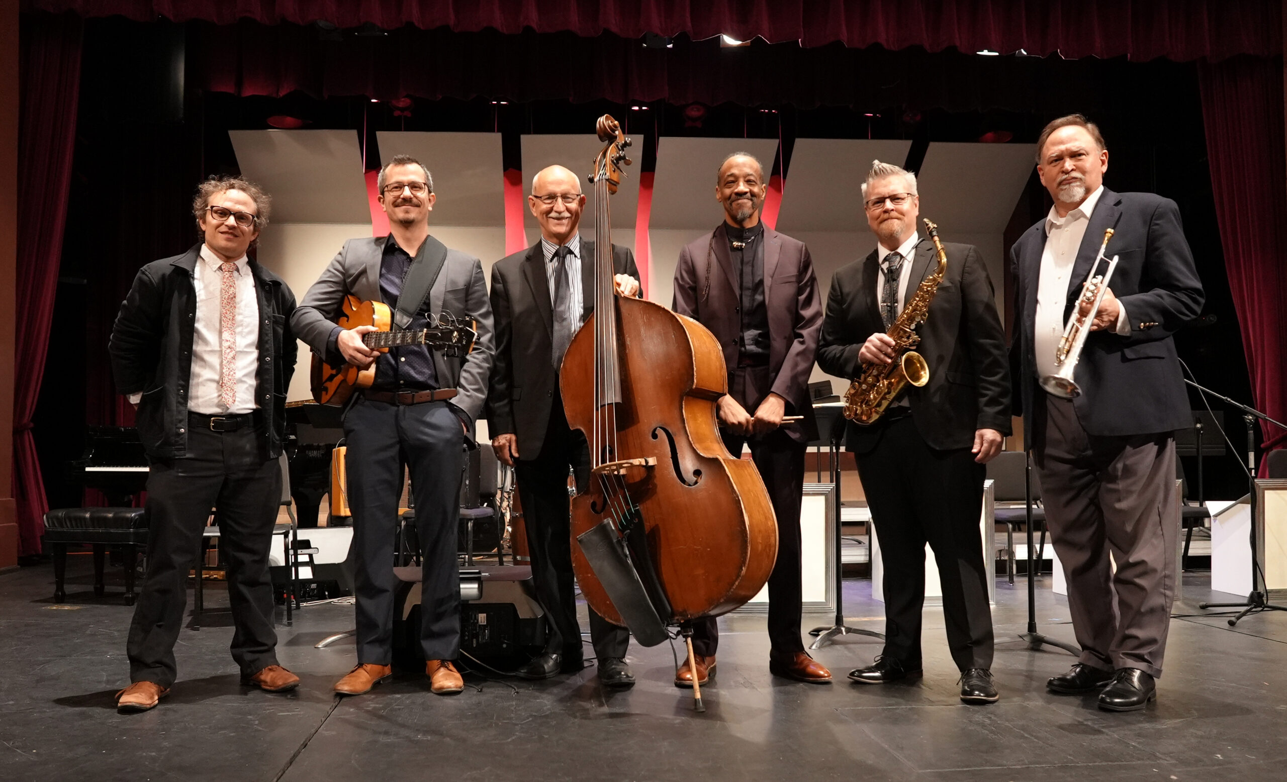 Six musicians standing on a stage with their instruments.