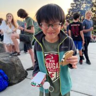 Student at outdoor picnic holding food.