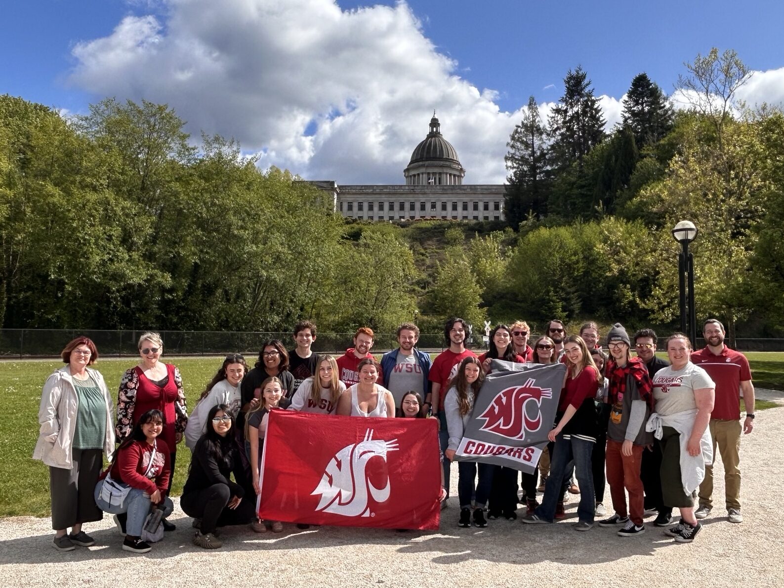 Large group photo of School of Music people standing outside of a capitol building, holding Coug flags.