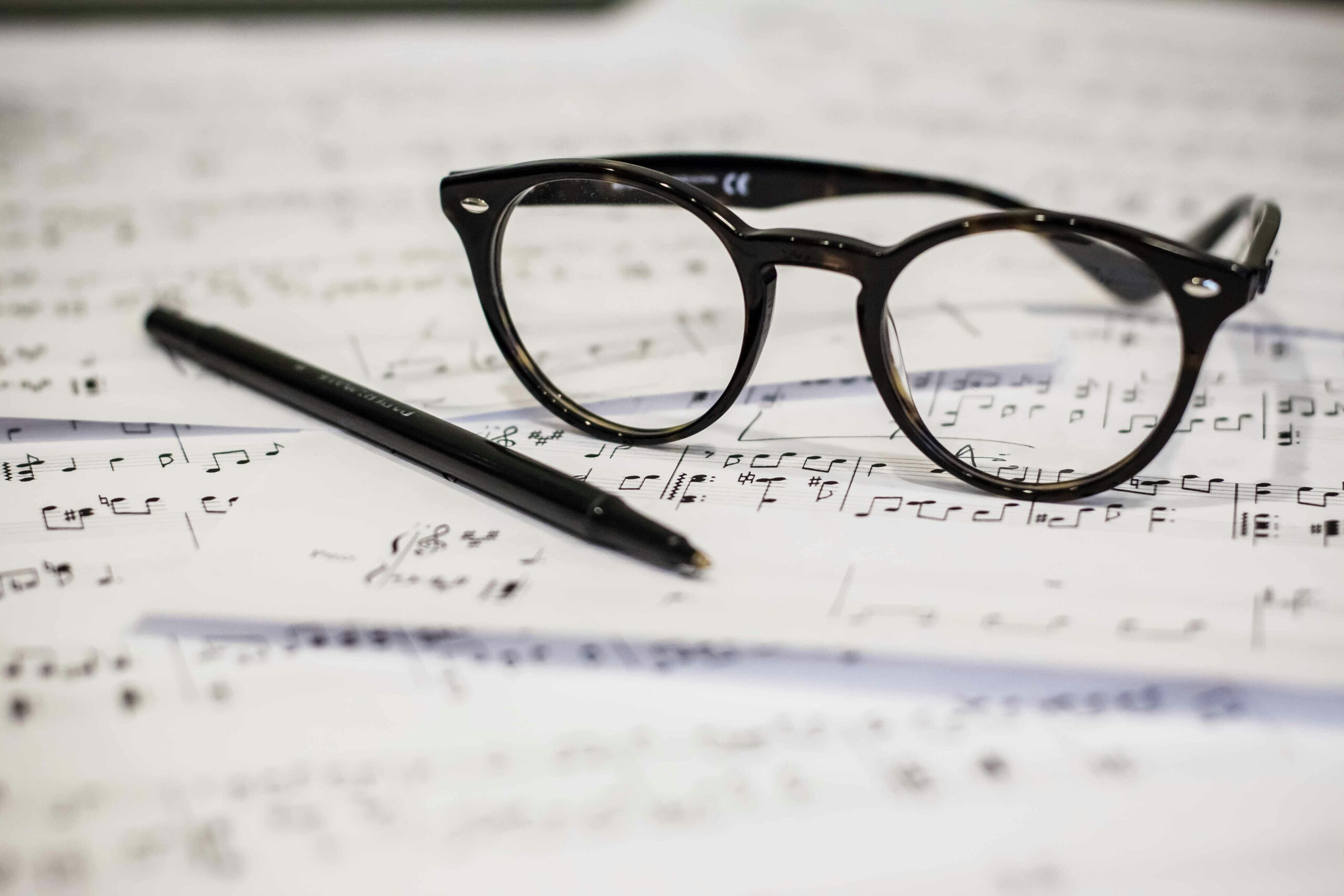 Musical notation strewn about a table, with pen and glasses.