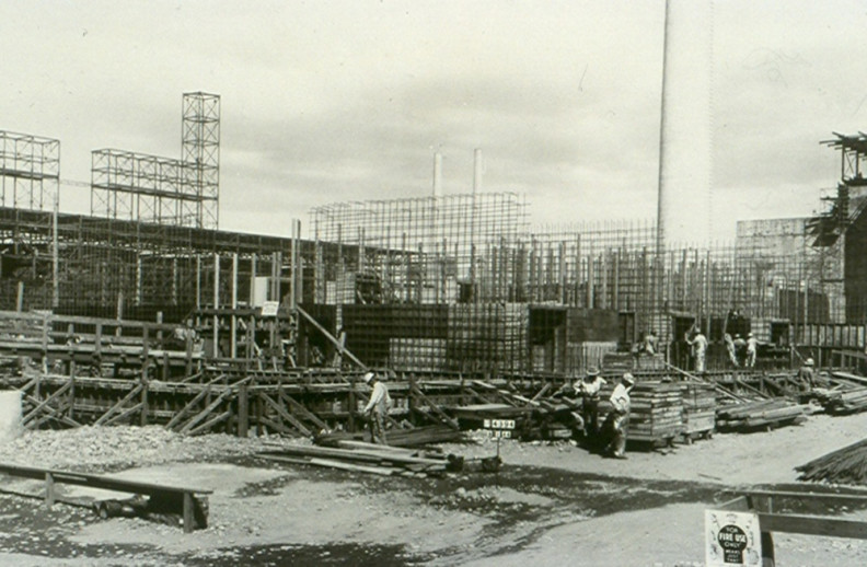 Crew members work among rebar, scaffolding, and equipment at a large construction site.